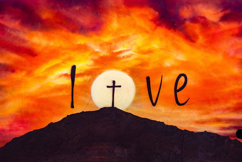 Street art of a sunset with the word “Love” and a cross.