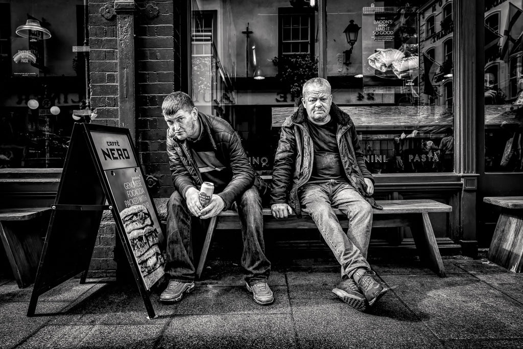 Two men, lost in thought outside a Dublin café, captured in a raw moment of urban life—unnoticed by the world rushing past.