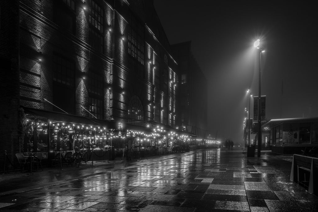 Capturing the quiet allure of Oslo at night with a wide aperture of f/2.8, allowing more light in and highlighting the reflections on the wet pavement—perfect for low-light street photography.