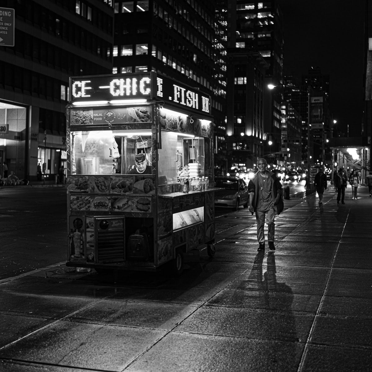 A Manhattan food vendor glowing beneath city towers at midnight.