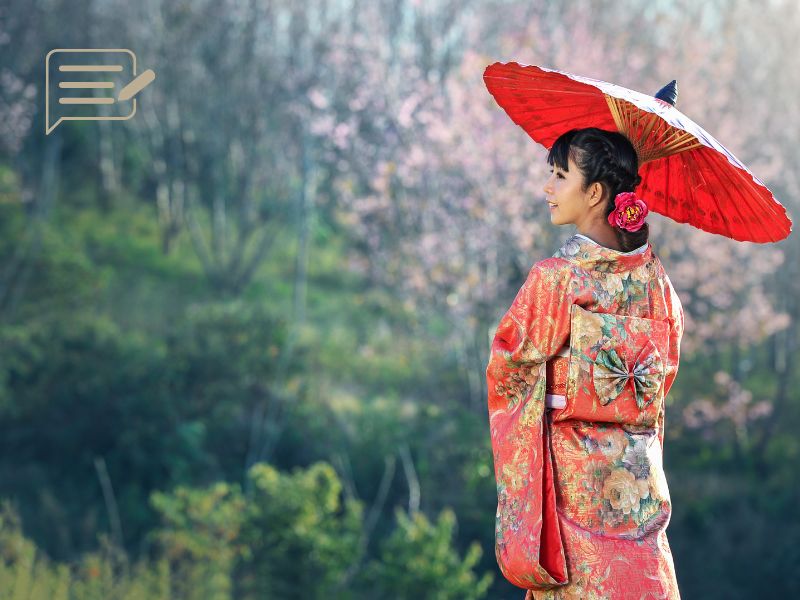 A woman dressed in a vibrant traditional kimono, holding a red umbrella amidst the backdrop of cherry blossoms in bloom.