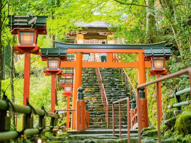 A bright red Torii gate standing proudly along a stone pathway, leading visitors through a lush forest to a tranquil shrine.